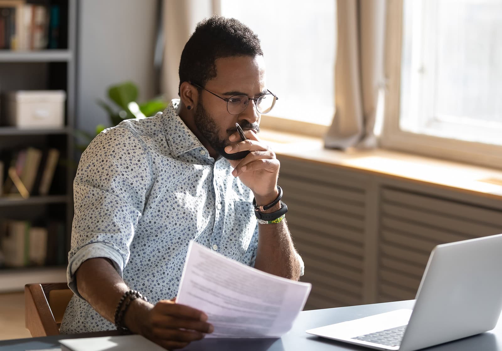 A man sitting at a computer while holding a piece of paper and thinking